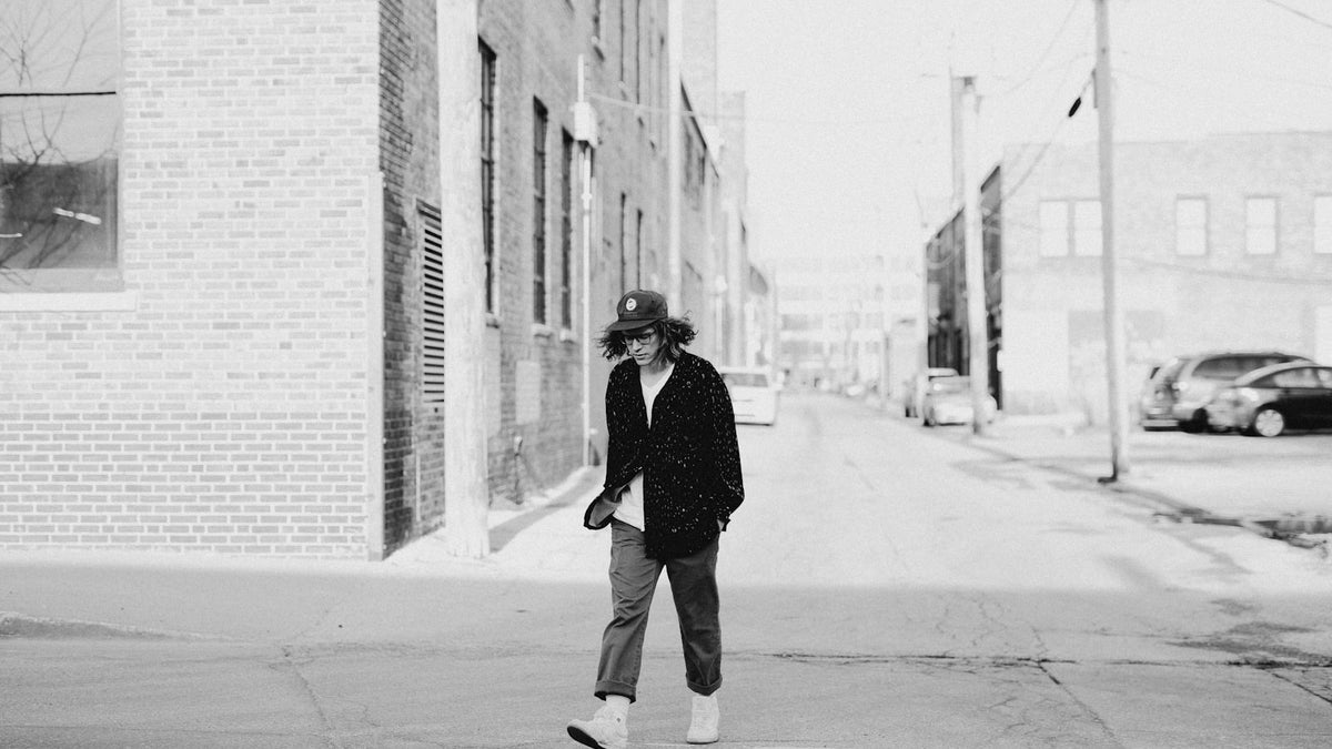 Grayscale editorial photo of a man walking alone down a city street, evoking the exit of Supreme's creative director
