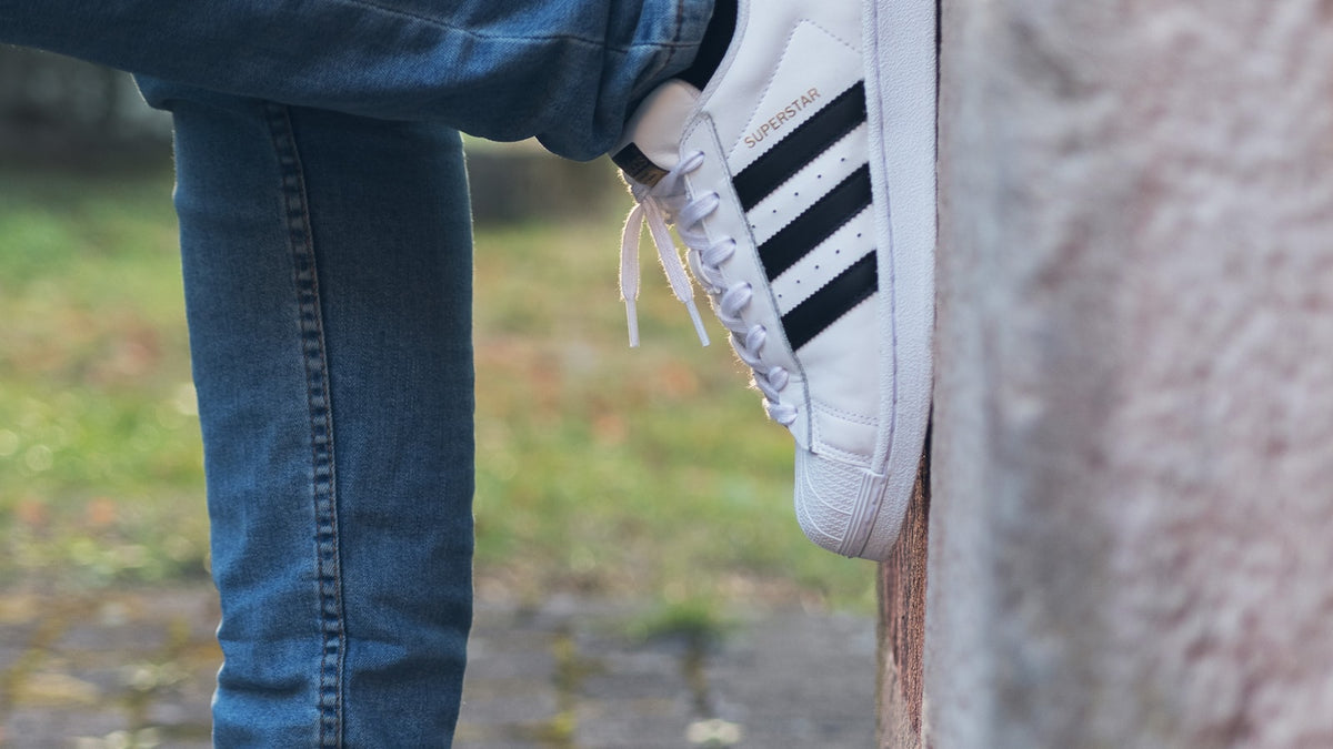 White adidas Superstar sneakers against a grey wall — the silhouette behind the Jennie x adidas collab