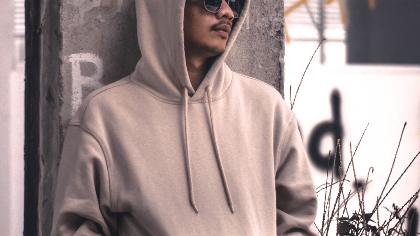How to style a hoodie: man in a grey hoodie leaning against an urban wall in daylight