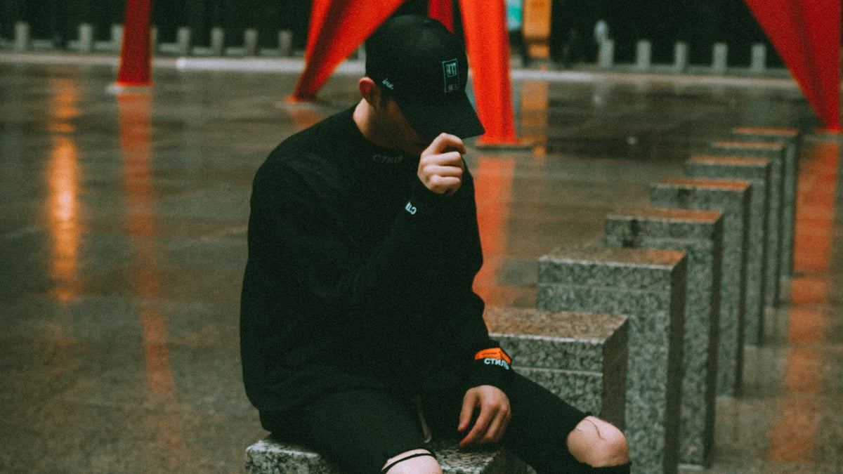 Stüssy Fall 2026 mood: monochrome street style with a black jacket and knit cap on a concrete bench