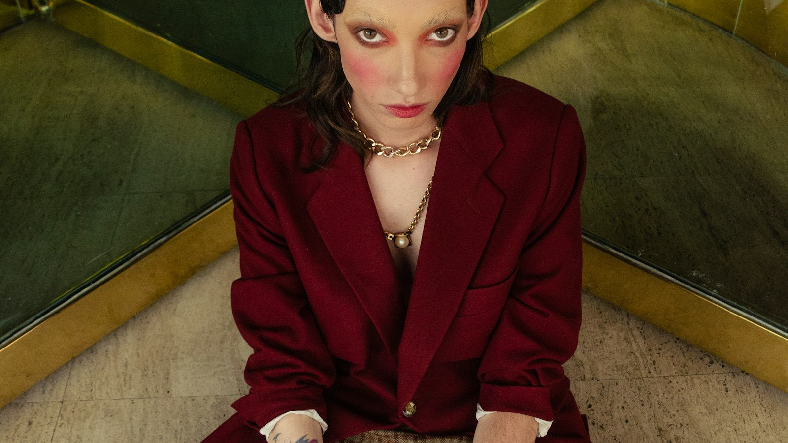 Woman in a red blazer seated on architectural stairs, an editorial fashion image evoking Donatella Versace's new brand era