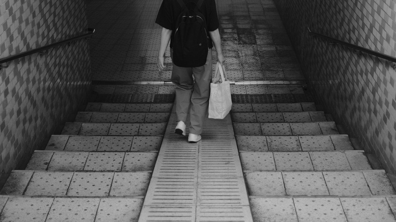 Tunnel fits: a lone figure in a dark jacket walking through a shadowed concrete tunnel, streetwear editorial style