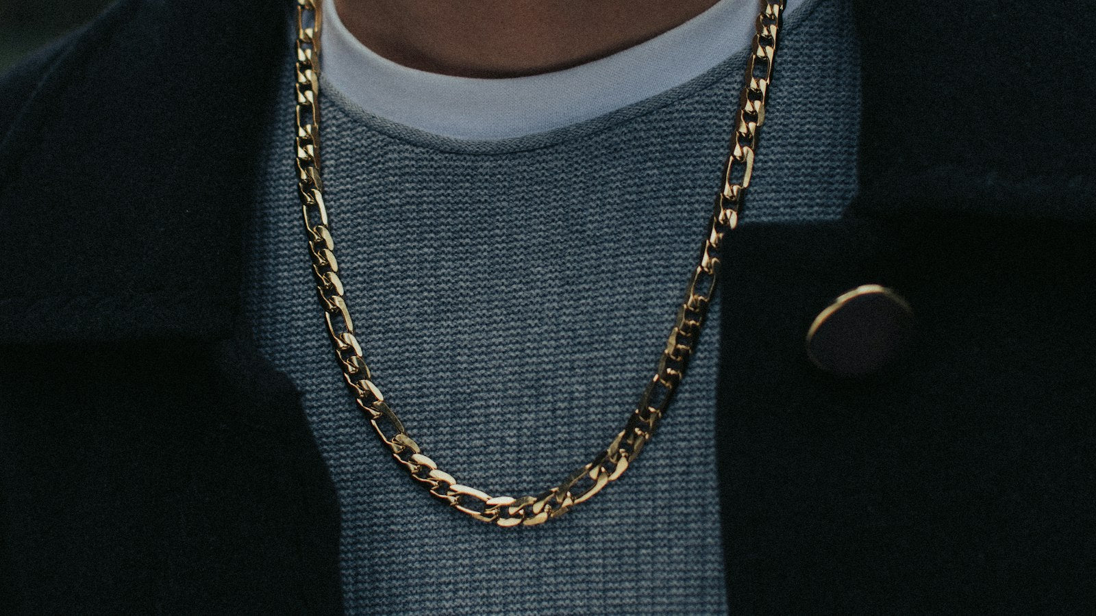 Man in a black coat showing how to wear a chain, gold necklace over dark streetwear