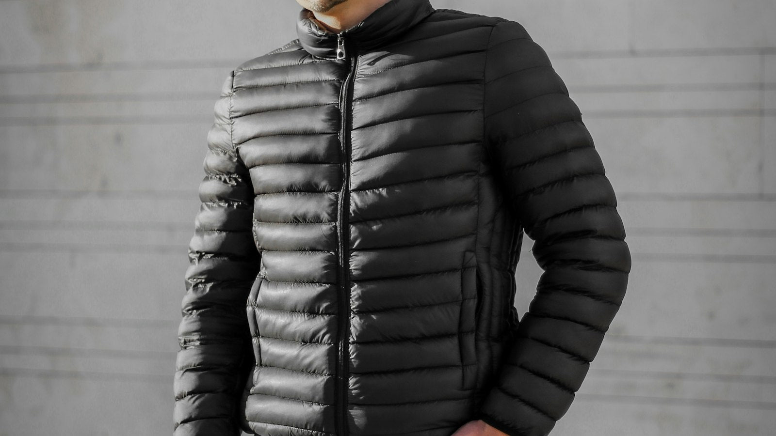 Man in a black puffer jacket standing against a grey concrete wall — how to style a puffer jacket