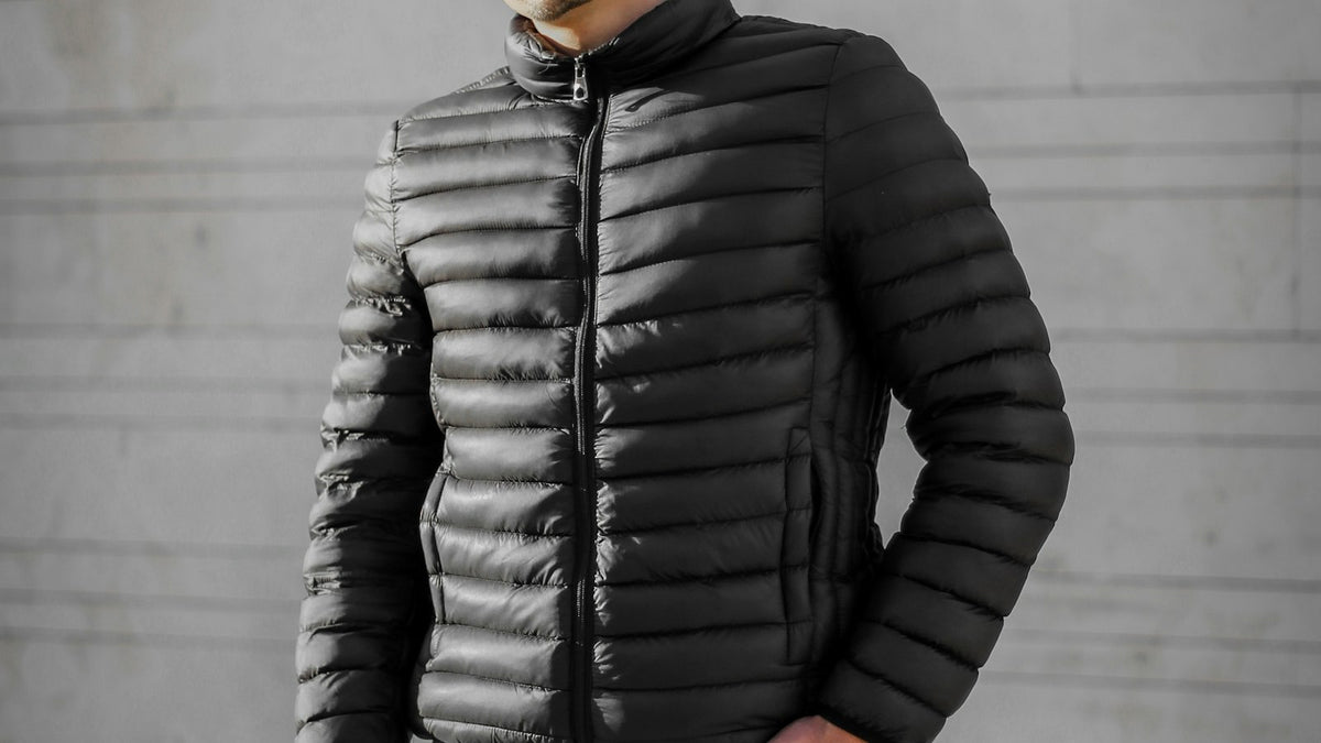 Man in a black puffer jacket standing against a grey concrete wall — how to style a puffer jacket