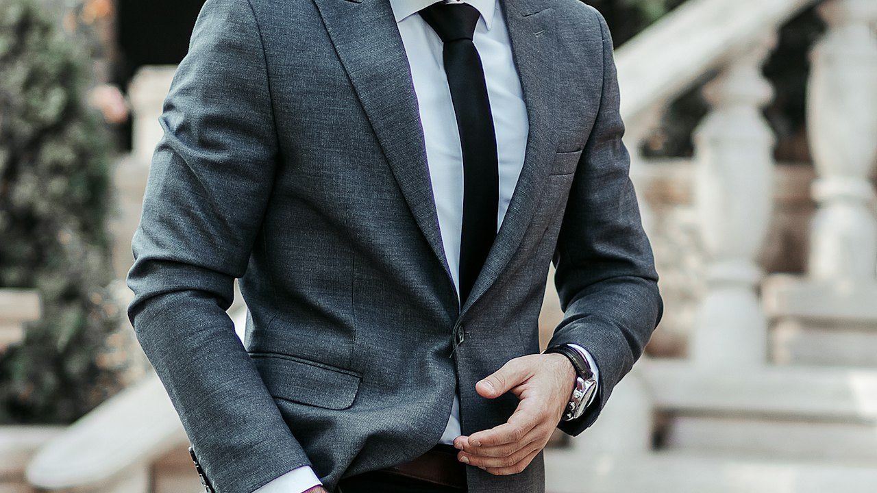 How to dress up streetwear: man in a tailored gray suit and sunglasses on concrete steps, moody editorial street style
