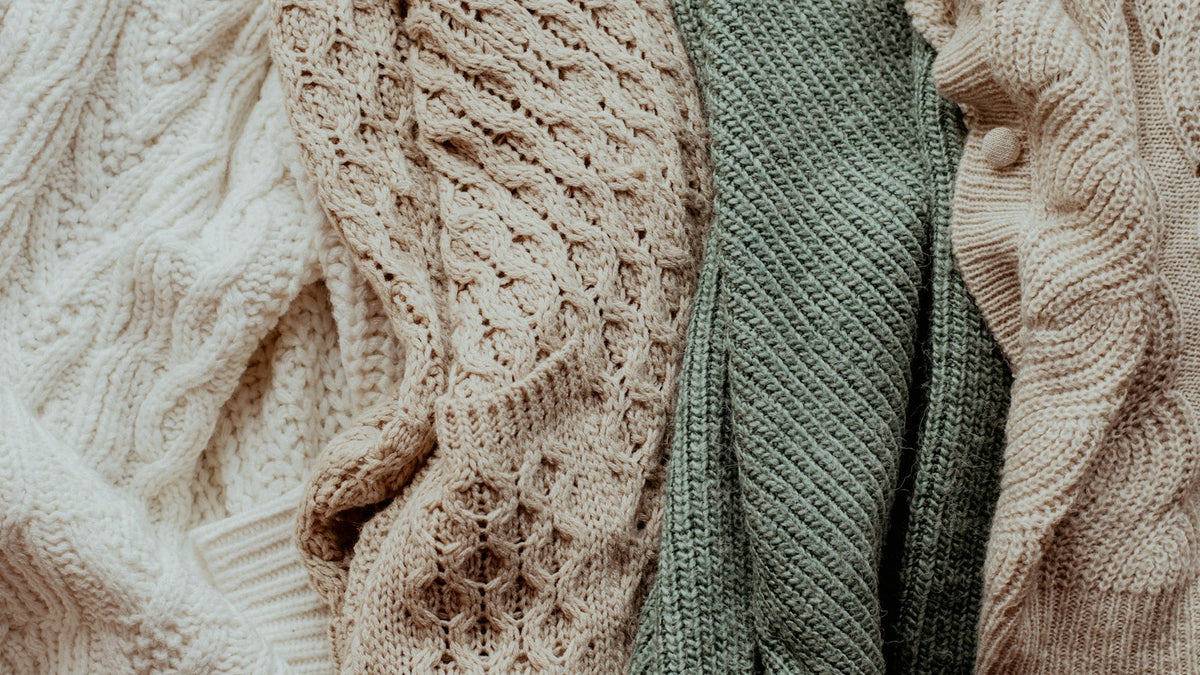 How to wash a sweater — folded knit sweaters stacked in muted autumn tones